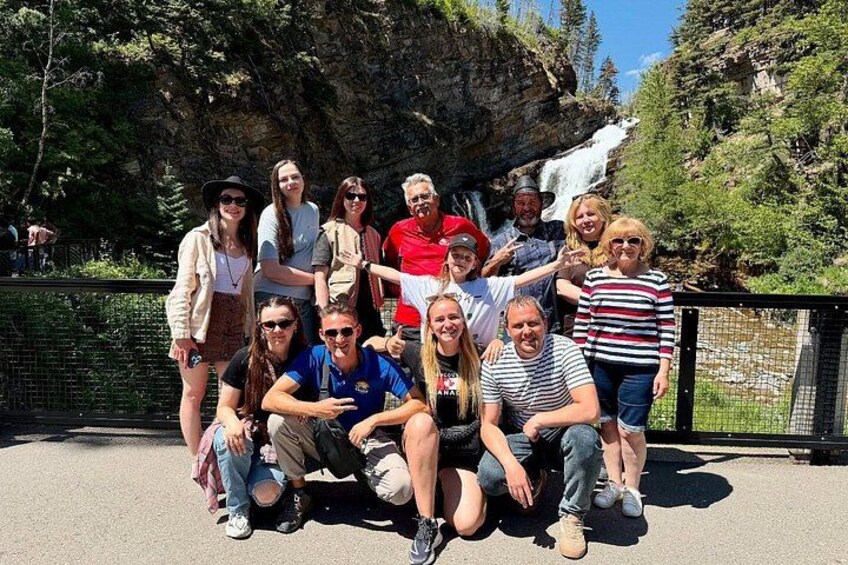 A group of people posing in front of a waterfall with a forested background. 2
