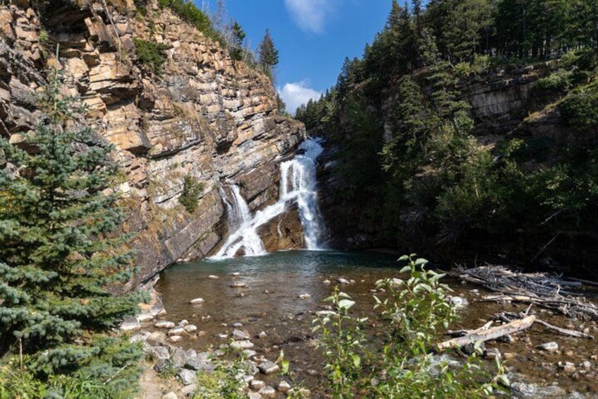 A waterfall cascading into a river surrounded by rocky cliffs and dense forest. 4