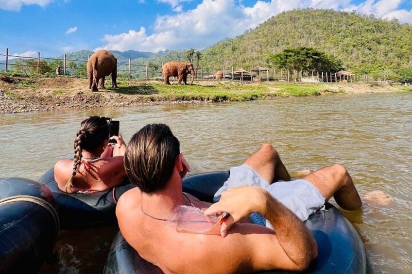 Two people on a raft in a river with elephants in the background. 1
