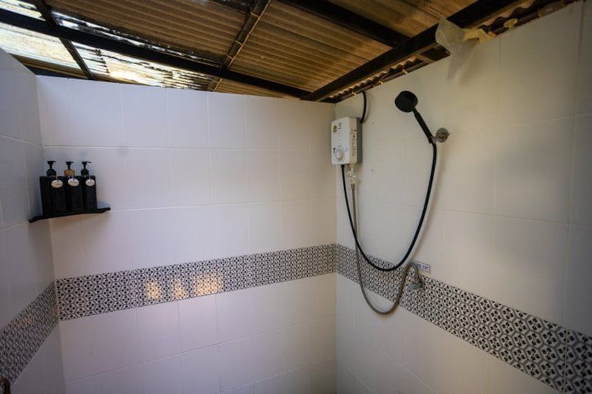 A shower area with tiled walls, a showerhead, and a shelf with bottles. 4