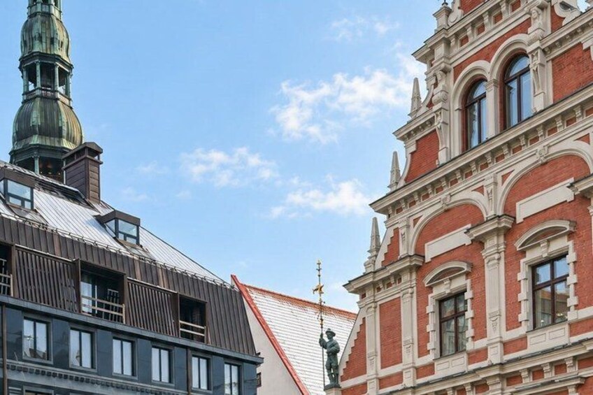 A building with a red facade and a green spire, a modern structure with a sloped roof, and a statue on the roof. 4