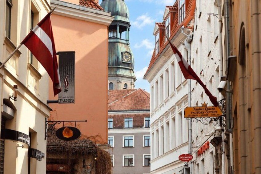 A street with buildings, a flag, and a sign for the Amber Queen Factory Outlet. 1