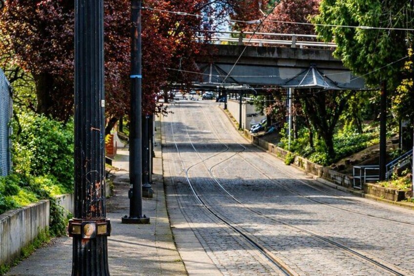 A street with tram tracks, a pedestrian sidewalk, and a bridge in the background. 5