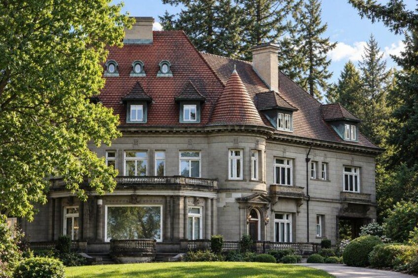 A large, historic stone building with a red-tiled roof, surrounded by lush greenery and trees. 4