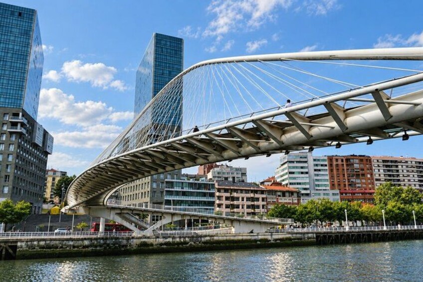 A modern bridge with a curved design, a river, and high-rise buildings in the background. 5