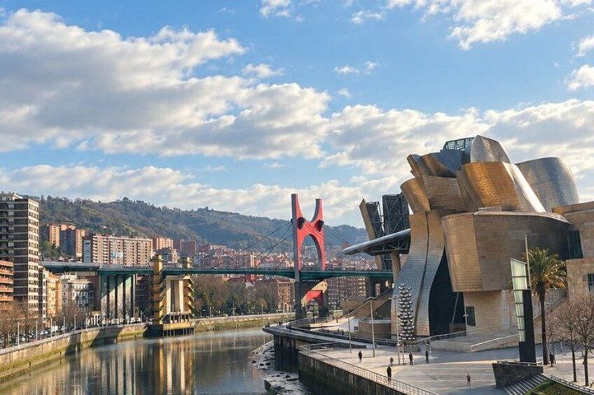 A river with a bridge, a modern building with a unique design, and a red sculpture. 3
