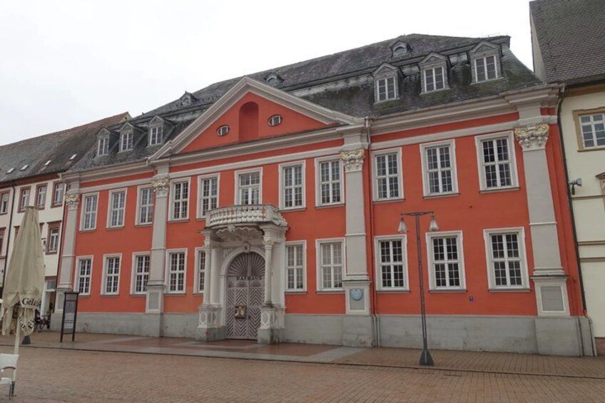 A red building with a white door and columns, a paved area in front, and a lamp post. 5