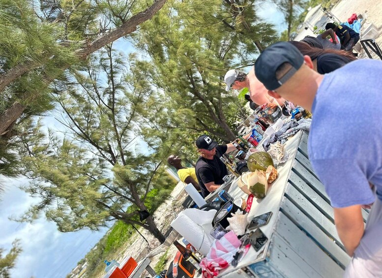Un groupe de personnes participe à un événement en plein air, autour d’une table remplie d’objets, et des arbres les entourent. 3
