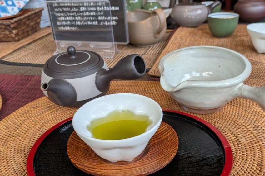 A teapot, a cup of tea, and a ceramic pitcher on a table with a placard. 2