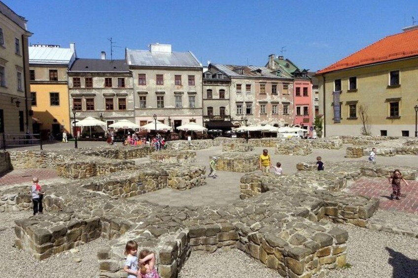 Ancient ruins with people walking around, surrounded by colorful buildings. 1