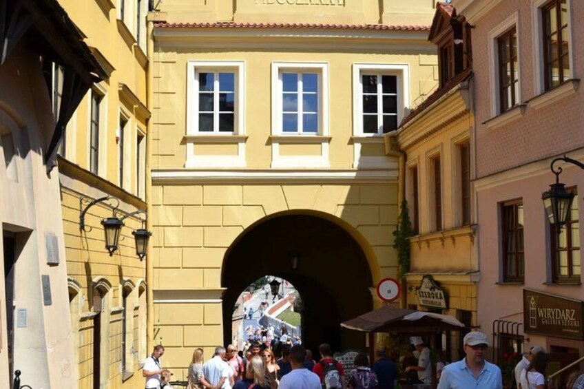 A street scene with a crowd of people, a yellow building with an arched entrance, and a sign for a store named 'WIRYDARZ'. 4