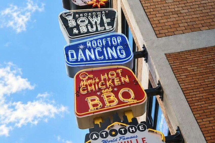 A row of neon signs advertising various local attractions including a bowling alley, rooftop dancing, and a BBQ restaurant. 2