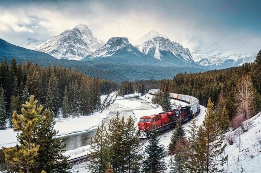 A red train traveling through a snowy forest with mountains in the background. 4