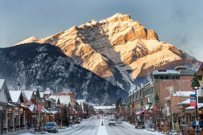 A snow-covered street in a town with buildings and a mountain in the background. 3