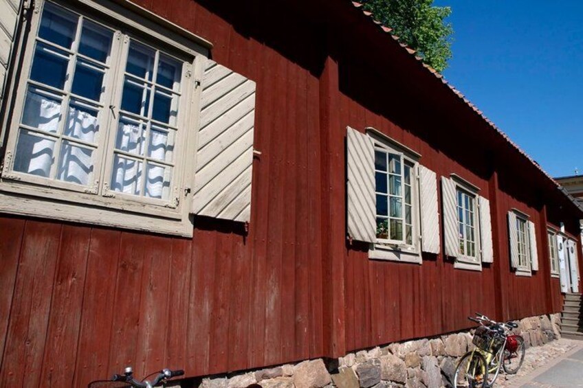 Un edificio de madera roja con contraventanas blancas, una bicicleta y cimientos de piedra. 4