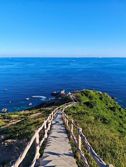 Un sentier côtier qui mène à la mer, avec des bateaux visibles au loin. 1