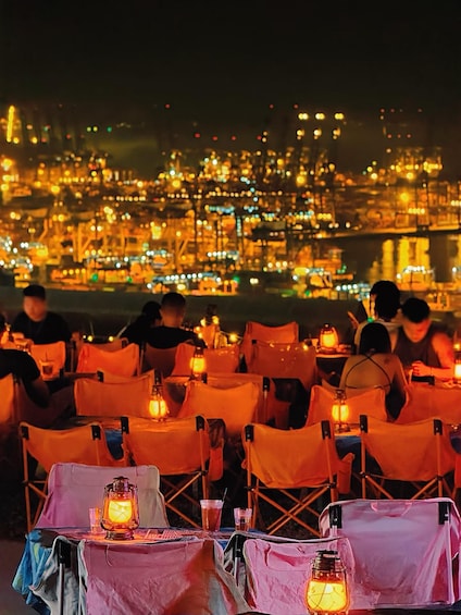 Un espace extérieur aménagé pour les repas en soirée, avec des tables et des chaises, éclairé par des lanternes, et offrant une vue sur un paysage urbain illuminé. 4