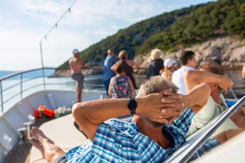 A boat with people relaxing on deck, a rocky coastline, and a clear sky. 2