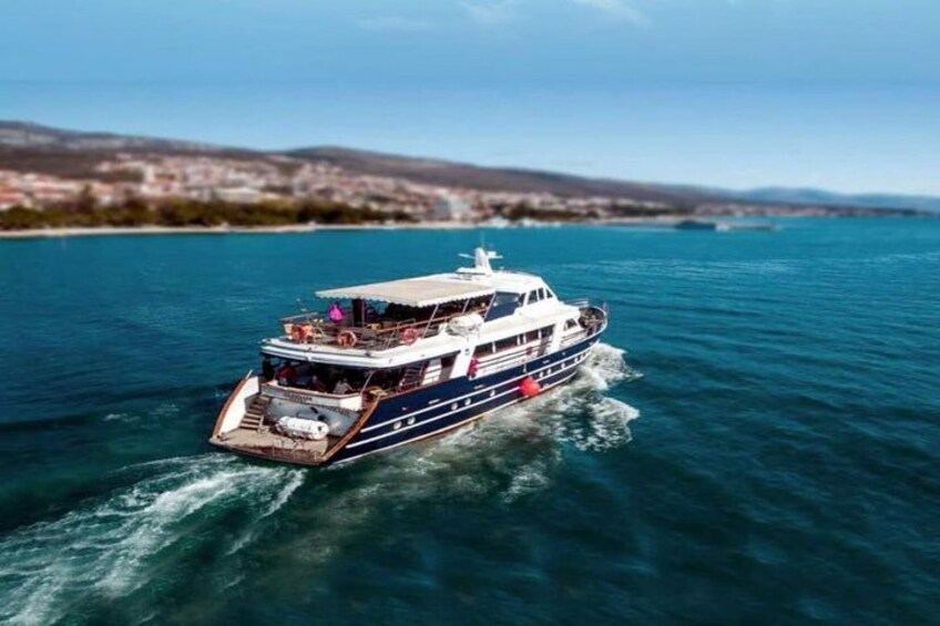 A large boat with multiple decks and passengers, cruising on a calm sea with a coastline in the background. 5