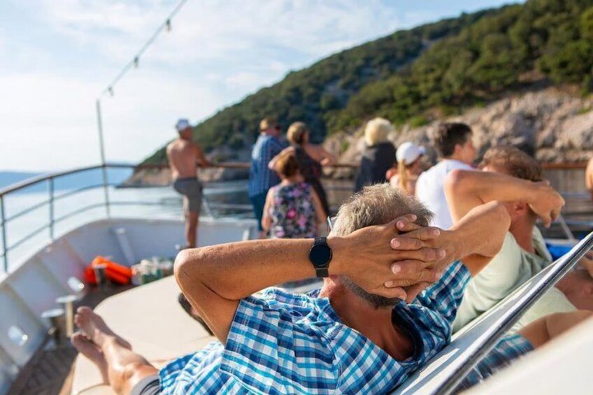 A boat with people relaxing on deck, a rocky coastline, and a clear sky. 1