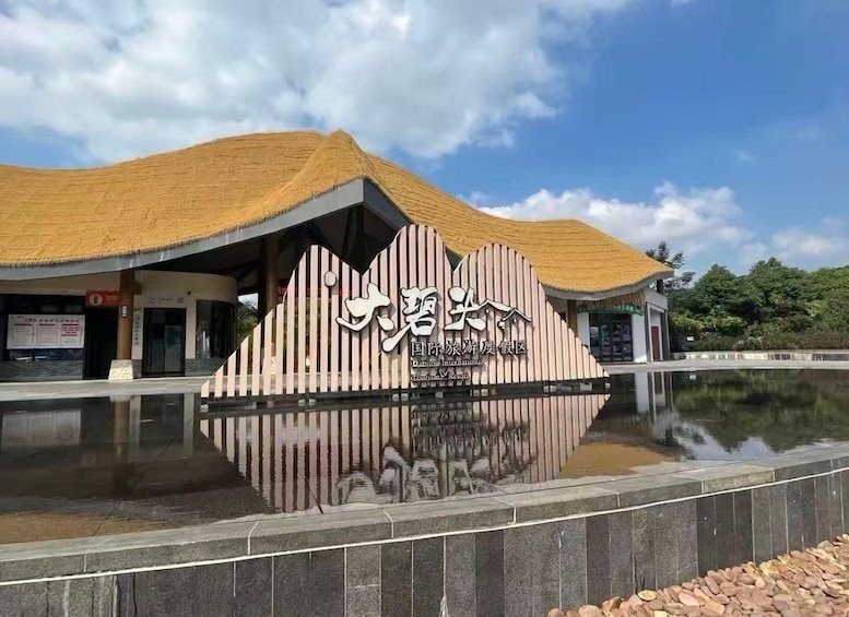 Un bâtiment à la façade rayée et au toit de chaume, dont le reflet se mire dans une étendue d’eau située devant. 1