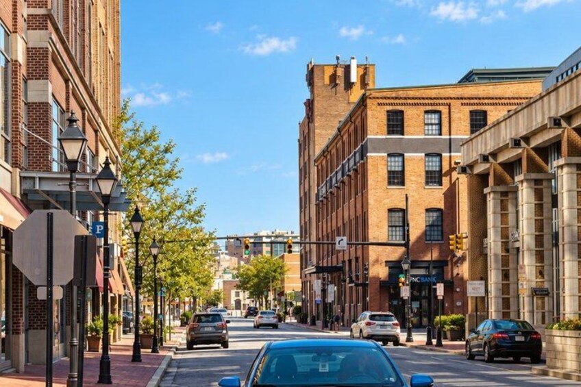 A street lined with brick buildings, cars parked along the curb, and a clear blue sky. 2