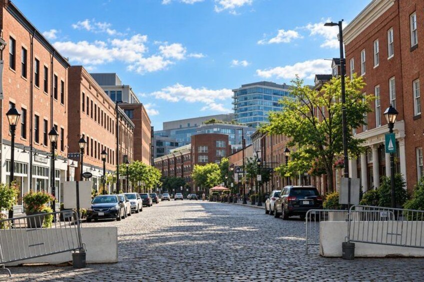 A cobblestone street lined with brick buildings, parked cars, and a clear blue sky. 3