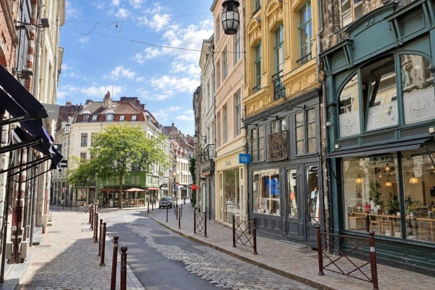A cobblestone street lined with historic buildings, a tree, and a café with outdoor seating. 2