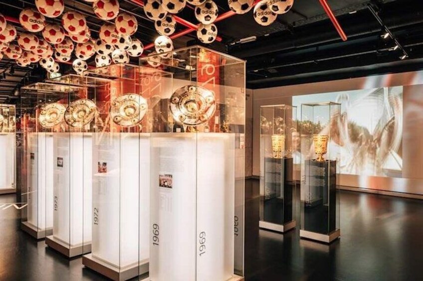 A museum exhibit with glass display cases containing historical soccer balls from 1972, 1969, and 1969. 3