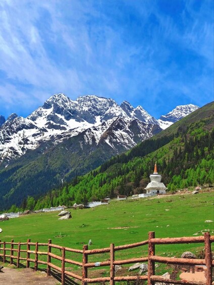 A mountain landscape with a snow-capped peak, a green valley, and a white stupa. 3