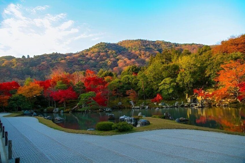 A serene lake surrounded by autumn foliage, with a pathway leading to a traditional Japanese garden. 2