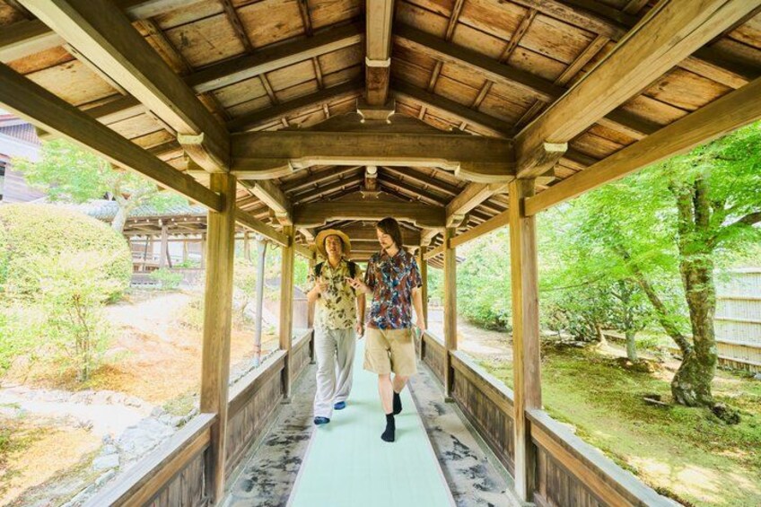A wooden bridge with a thatched roof, surrounded by greenery and trees. 5