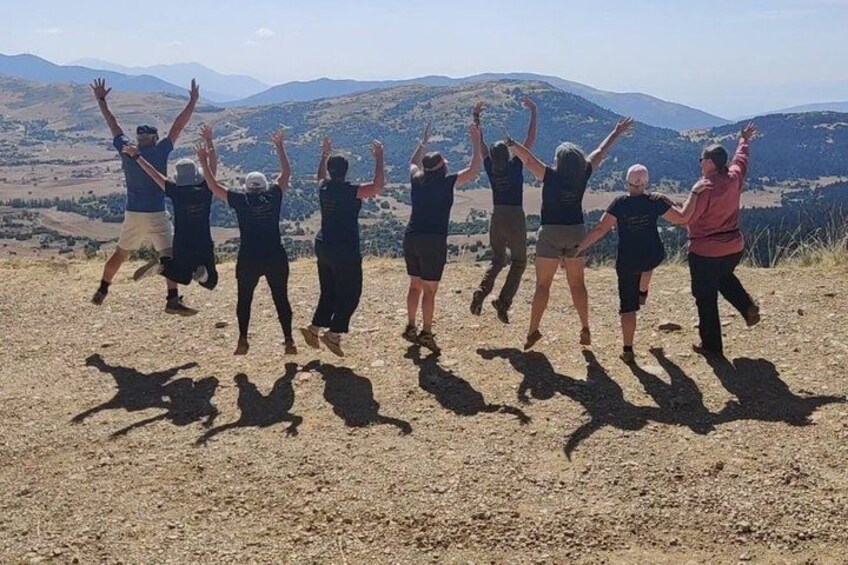 A group of people jumping in a line on a dirt path with a mountainous landscape in the background. 3