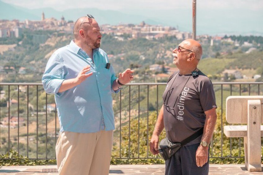 Two men standing on a balcony overlooking a cityscape. 5