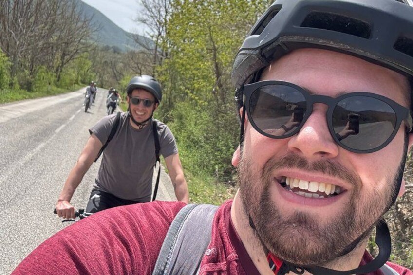 A person on a bicycle on a road with trees and mountains in the background. 2