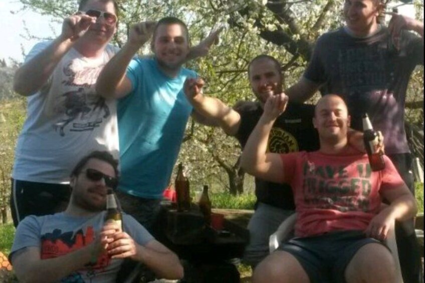 A group of people outdoors, some holding bottles, with trees and a picnic table in the background. 4