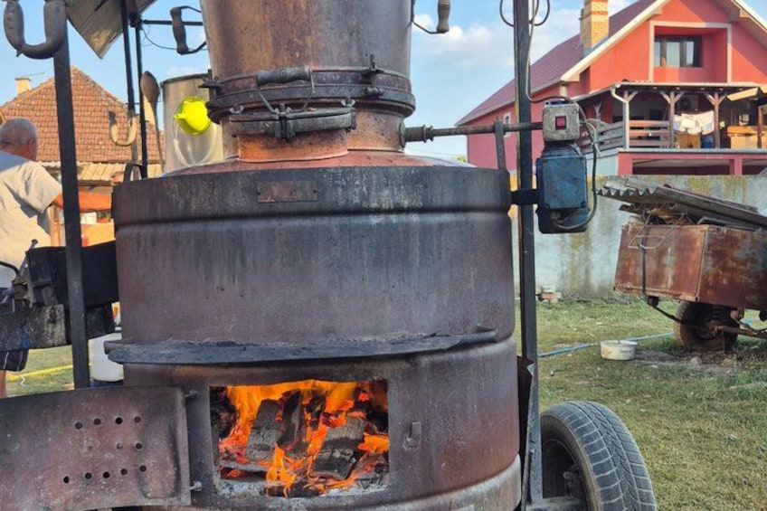 A large industrial boiler with visible flames, a yellow safety light, and a red building in the background. 1