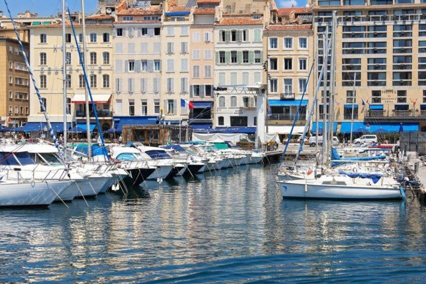 A marina with multiple sailboats docked, a waterfront promenade, and buildings with balconies. 2