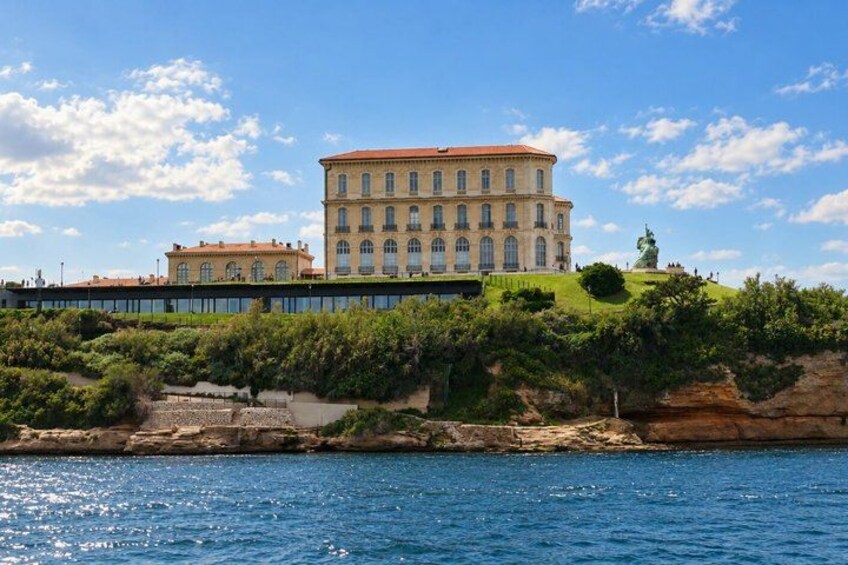 A large building with a red roof, situated on a grassy hill overlooking a body of water. 4