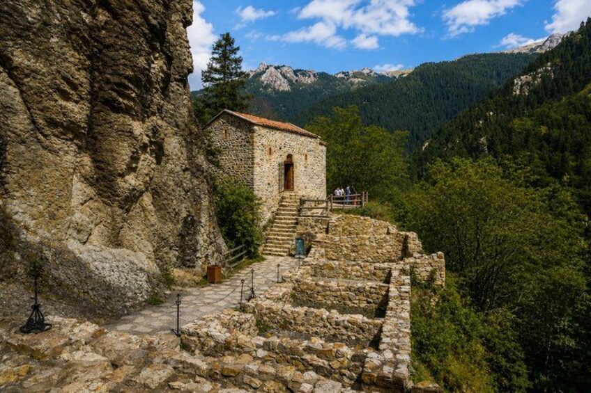 A stone building with a red-tiled roof, surrounded by a stone wall and a staircase leading up to it. 5