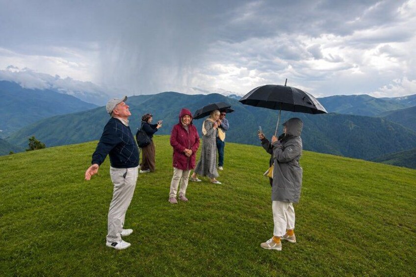 A group of people on a grassy hill with a mountainous landscape in the background. 2