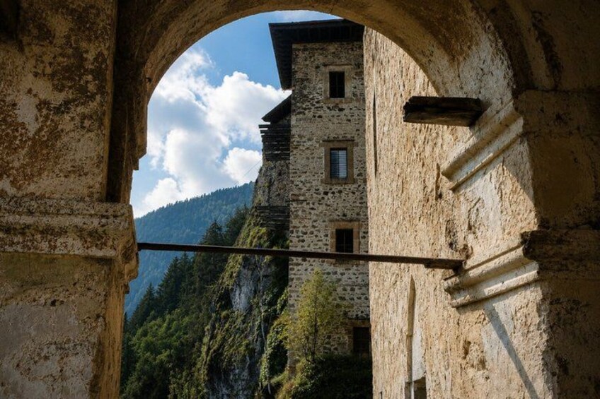 An arched stone structure with a view of a mountain and a building. 3