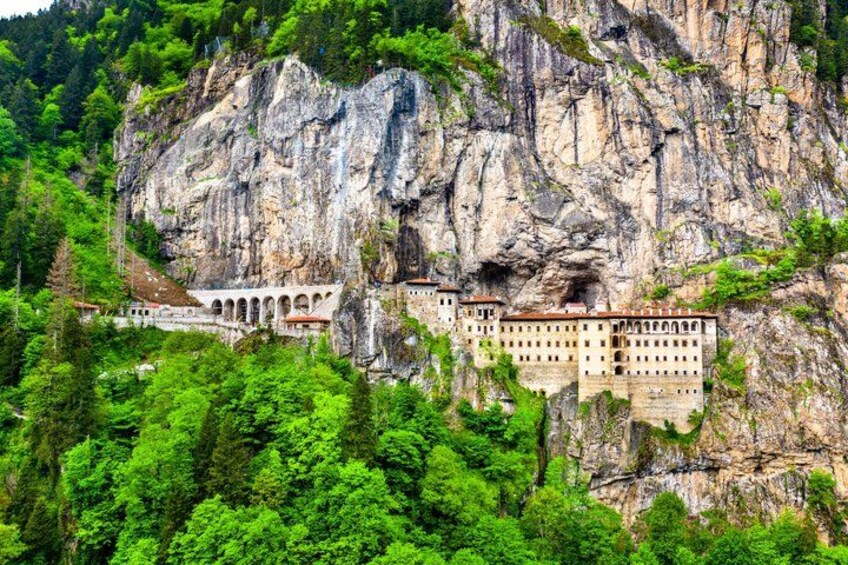 A monastery built into a cliffside, surrounded by lush greenery. 1
