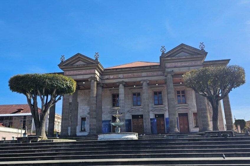 A large, historic building with columns and a fountain in front. 1