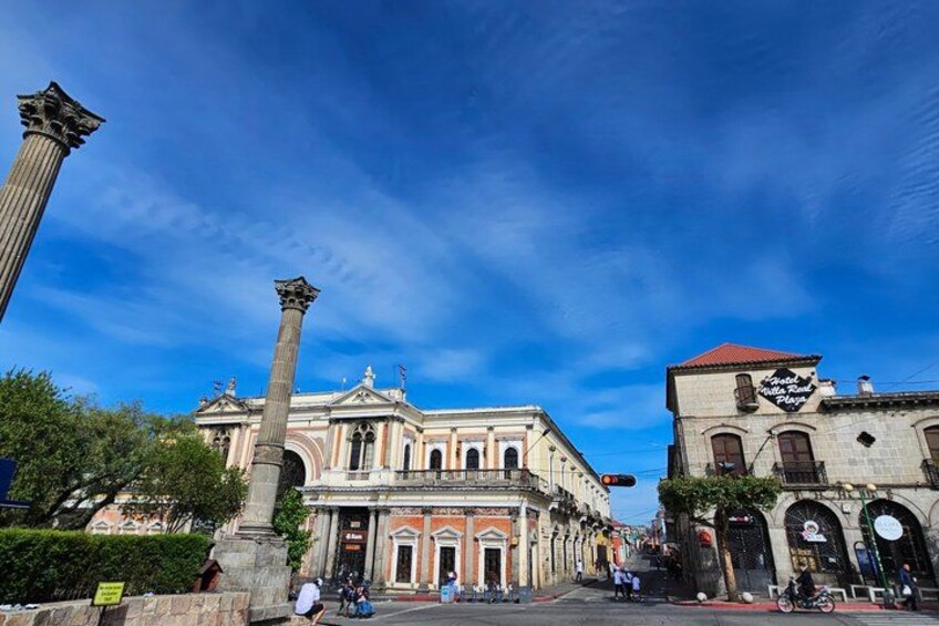 A historic building with columns, a red-roofed structure, and a clear blue sky. 3