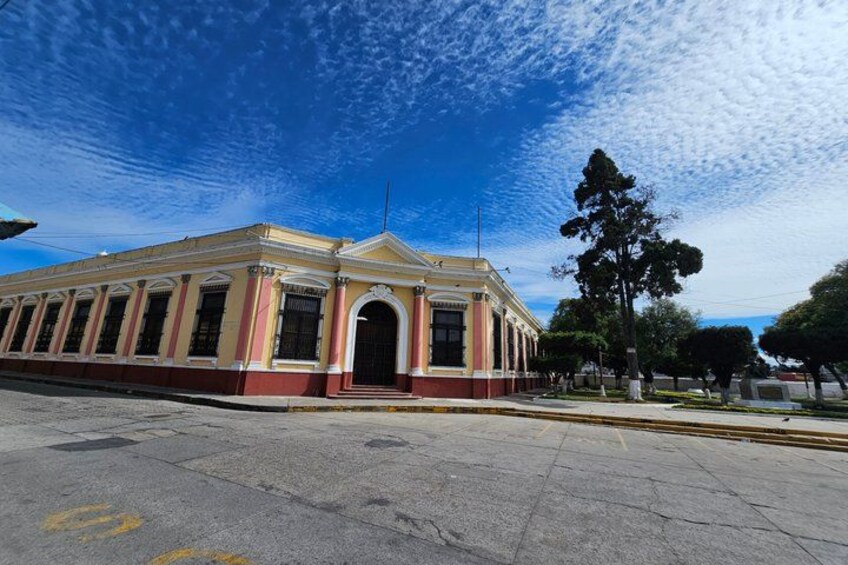 A large, historic building with a red and yellow facade, arched windows, and a central entrance. 4