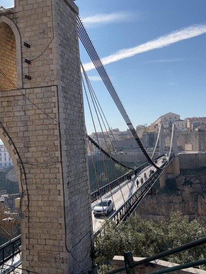 A suspension bridge with a stone tower, vehicles on the road, and buildings in the background. 5