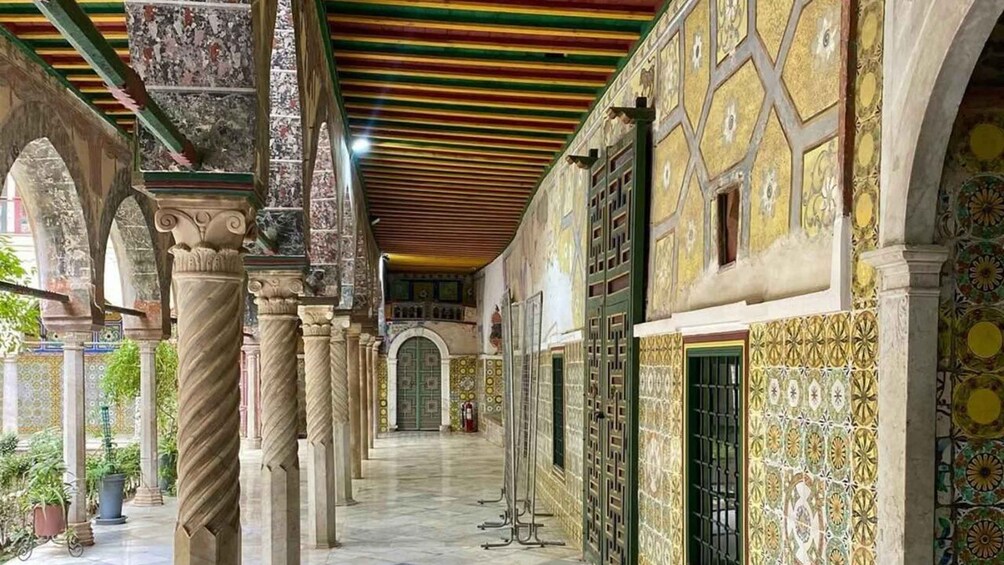 Un couloir couvert, orné de colonnes décoratives, de murs aux motifs élaborés et d’un sol carrelé. 2
