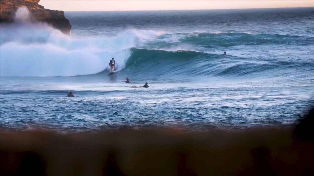 A surfer riding a wave, other surfers in the water, and a rocky coastline. 4