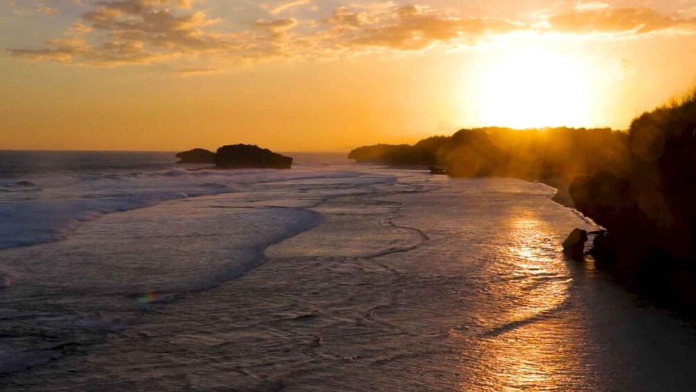 A beach at sunset with waves, a rocky outcrop, and a clear sky. 2